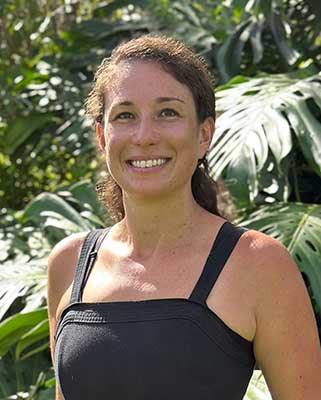 Rachel Erdman, Food Safety Specialist at NSEVP, smiling outdoors in front of tropical foliage.